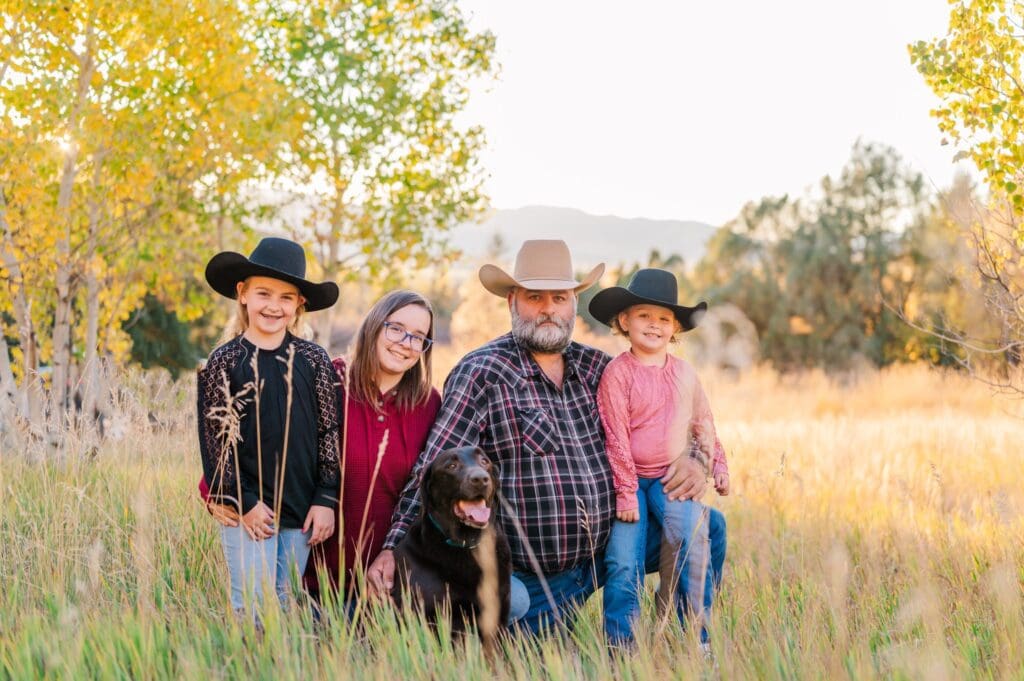 Family of four standing together in the Caribou National Forest during fall, surrounded by golden leaves and soft mountain light. Captured by a Grace, Idaho family photographer, the photo shows genuine laughter, love, and connection in the heart of Southeastern Idaho.